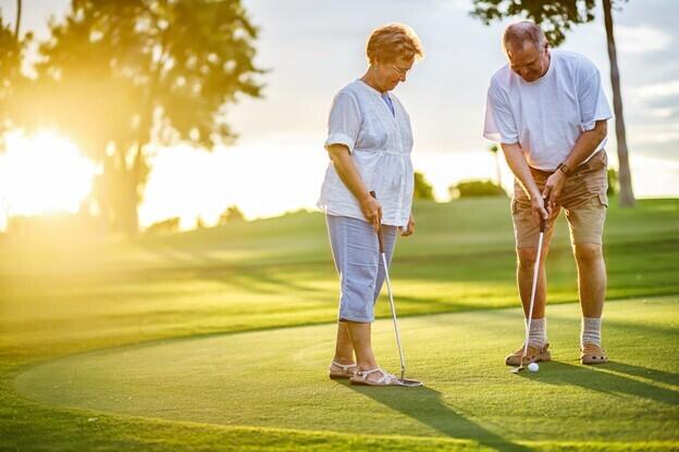 older woman stands on golf green beside an older man who is putting