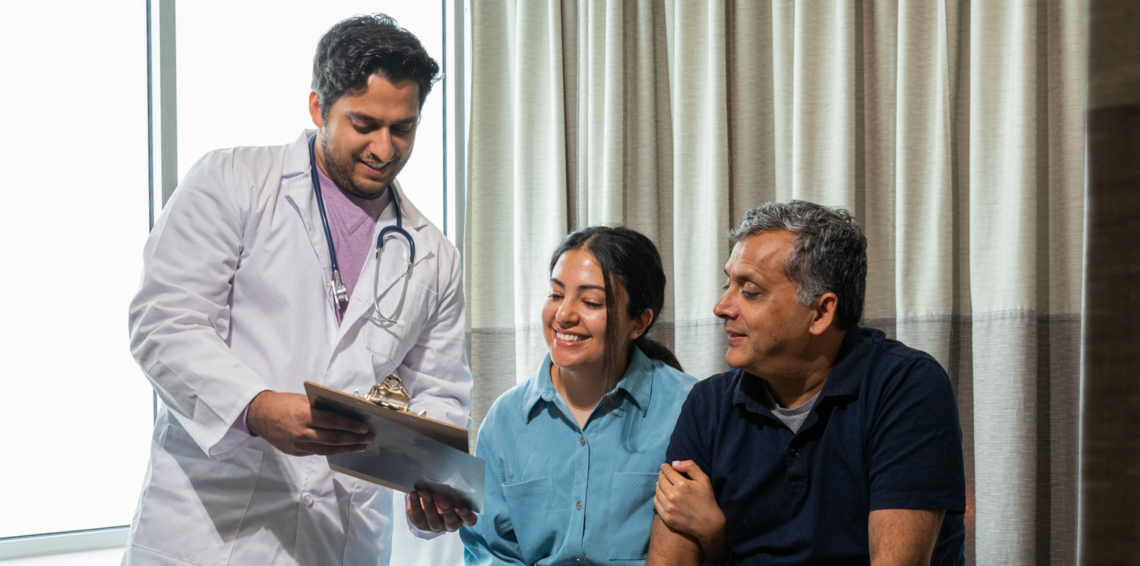 Doctor stands holding a clipboard talking to an older patient and their daughter